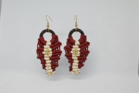 Pair of macrame earrings with red, gold, and white design on a gray background